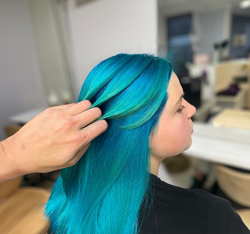 Stylist holding a section of vibrant teal-blue dyed hair at Salon Deelegance