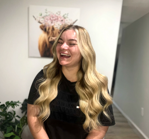 Smiling client with long wavy blonde balayage hair at Salon Deelegance, Penrith