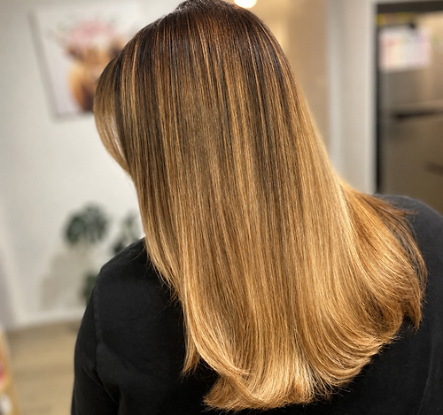 Warm blonde and caramel balayage highlights on long hair at Salon Deelegance
